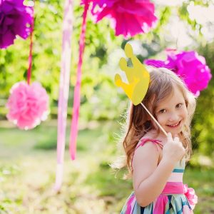 Girl smiling with paper crown outdoors.
