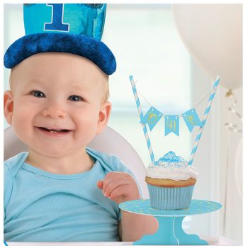 Smiling baby boy celebrating first birthday with blue hat and cupcake.