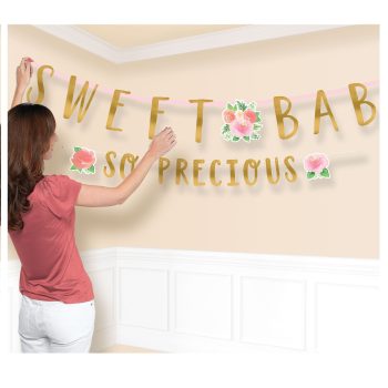 Woman hanging colorful "Sweet Baby So Precious" banner on wall.