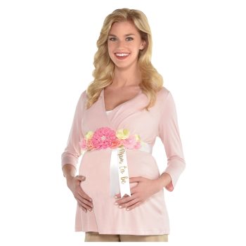 Smiling pregnant woman gently holding her belly, wearing a pink top and beige pants.