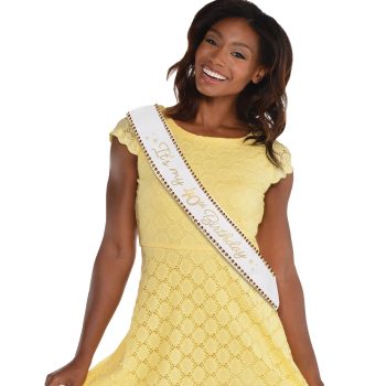 Smiling woman in yellow dress with sash.