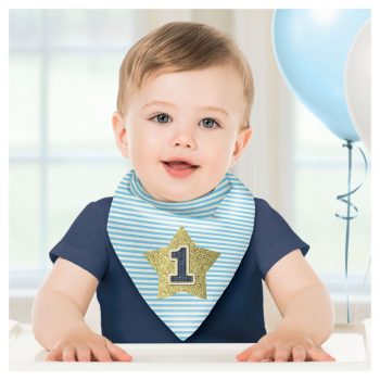 A smiling baby boy wearing a striped bib with a number 1 on it, sitting with balloons in the background.